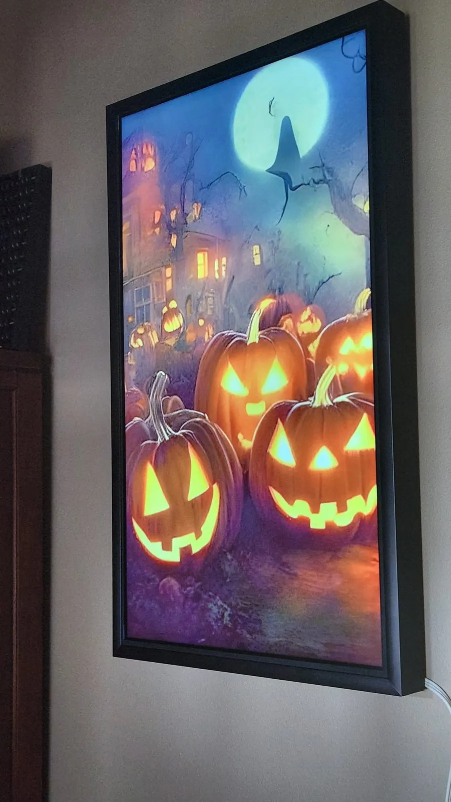 A black portrait frame on a wall showing an illustration of glowing jack-o
